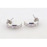 A pair of half hoop ear studs, each set with baguette cut glass centres, on white metal plain