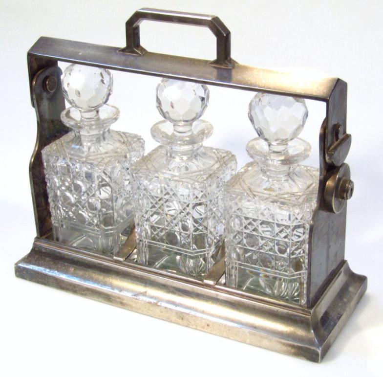 A mid-20thC metal cased three bottle tantalus, the shaped outline set with three cut glass decanters