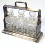 A mid-20thC metal cased three bottle tantalus, the shaped outline set with three cut glass decanters