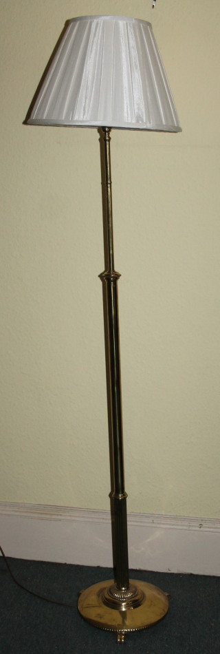 An early 20thC brass floor lamp, of cylindrical form on a circular base with three moulded feet, and