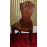 A George III mahogany hall chair, with a shield shaped back, a serpentine solid seat on square