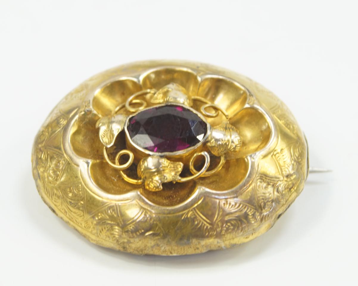 A Victorian memorial brooch, set with a garnet, hair filled memorial window verso in yellow metal.