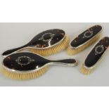 A George V silver and tortoiseshell four piece dressing table set, comprising of two hairbrushes