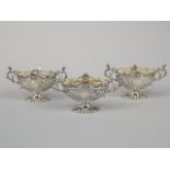 A set of three late Victorian silver salts, each with two handles, and embossed with scrolls, etc,