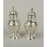 Two similar George VI silver baluster shaped pepper pots, each with a turned finial, on a domed