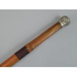 An early 20thC cane Koshe stick, having white metal top with foliate scroll decoration leading to