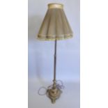 An early 20thC brass standard lamp, with reeded column, lobed base with bun feet, and a green