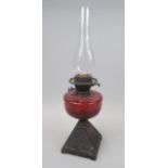 A Victorian oil lamp, with a ruby tinted reservoir and a cast iron base, 58cm high overall.