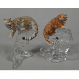 Two porcelain models, one in the form of a leopard, the other a tiger, each on a moulded glass