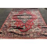 A 20thC machine woven rug, in floral geometric pattern, predominantly in blue and red, 210cm wide.