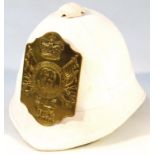 A 20thC pith helmet, in white material, fronted by a highly decorative brass plaque with part fitted