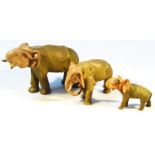 A graduated set of three early 20thC bisque figures of elephants, each with trunks raised,