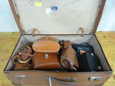 A quantity of binoculars and cameras in a vintage suitcase