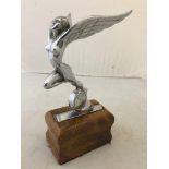 A vintage car accessory mascot in the form of a winged nude figure leaning forward, stood on a