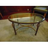 Oval glass top coffee table the top mounted on a forged and painted metal base with a scroll pattern