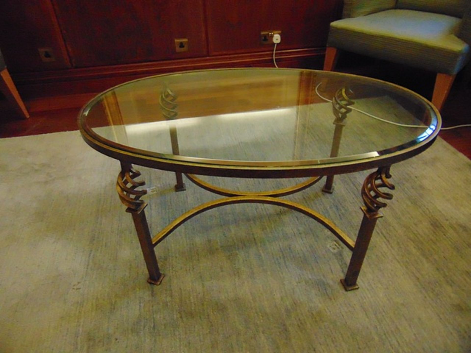 Oval glass top coffee table the top mounted on a forged and painted metal base with a scroll pattern