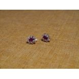 A pair of ruby and colourless stone cluster earrings, the oval cut ruby within a band of stones,