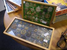 A collection of British military cap, shoulder and cross-belt badges, mounted in two frames,
