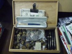 A box of mixed currency, military buttons and fountain pens