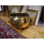 A large brass cauldron-form log bin, with swing handle and hammered finish and raised on paw feet.