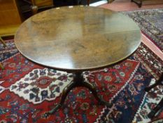 An antique oak tilt top table with a well coloured 74 cms diameter top on a turned column tripod