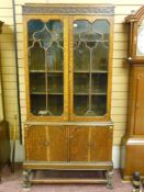 A circa 1930's oak bookcase having a stepped top over a carved frieze, twin glazed top doors with