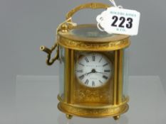 A small oval brass cased carriage clock with chased decoration, white enamel circular dial set