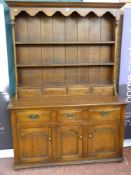 A reproduction oak dresser, the three shelf plate rack with planked back and shaped frieze under a