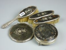A four piece silver and tortoiseshell dressing table set of hand mirror, two narrow brushes and