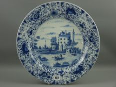 A mid 19th Century blue and white Delft pottery charger with a central scene of a castle with men in