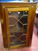 A mahogany single door hanging corner cupboard with astragal glazed door and shaped interior