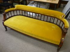 An Edwardian carved mahogany salon settee, the curved spindle gallery back with padded upholstered