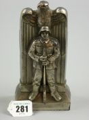 A cast white metal statue of a World War II German sentry standing before a plinth with