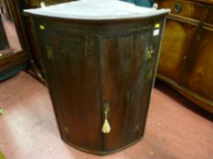 An antique crossbanded oak two door bow front hanging wall cupboard with brass hinges and escutcheon