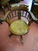 An Edwardian oak swivel captain's chair with cane work seat, spindle gallery back with carved