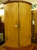 A light oak craftsman made reproduction two door bow front hanging corner cupboard with brass 'H'
