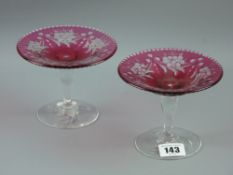 A pair of small cranberry tazza with wheelcut floral decoration on clear glass footed stem bases