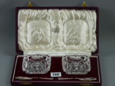 A cased pair of cut glass butter dishes with a pair of hallmarked silver butter knives, Birmingham