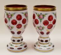A PAIR OF BOHEMIAN OVERLAID CRANBERRY GLASS GOBLETS decorated with flowers and gilding, 17cms