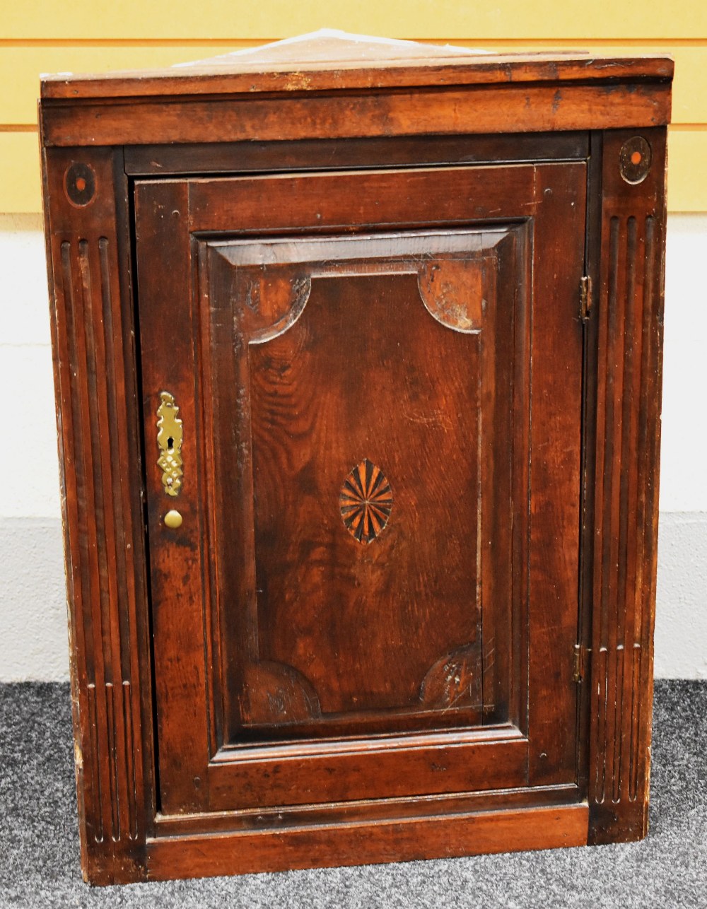 AN ANTIQUE HANGING CORNER CUPBOARD with brass fittings and inlaid centre cartouche to door and