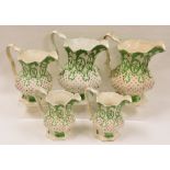 A SET OF FIVE NINETEENTH CENTURY STAFFORDSHIRE JUGS each of faceted form and with green and red