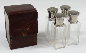 A VINTAGE LEATHER-CASED TRAVELLING SCENT BOTTLE SET comprising four square based clear glass bottles