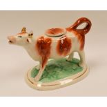 A NINETEENTH CENTURY STAFFORDSHIRE RED AND WHITE COW CREAMER on an oval painted and gilded base,