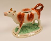 A NINETEENTH CENTURY STAFFORDSHIRE RED AND WHITE COW CREAMER on an oval painted and gilded base,