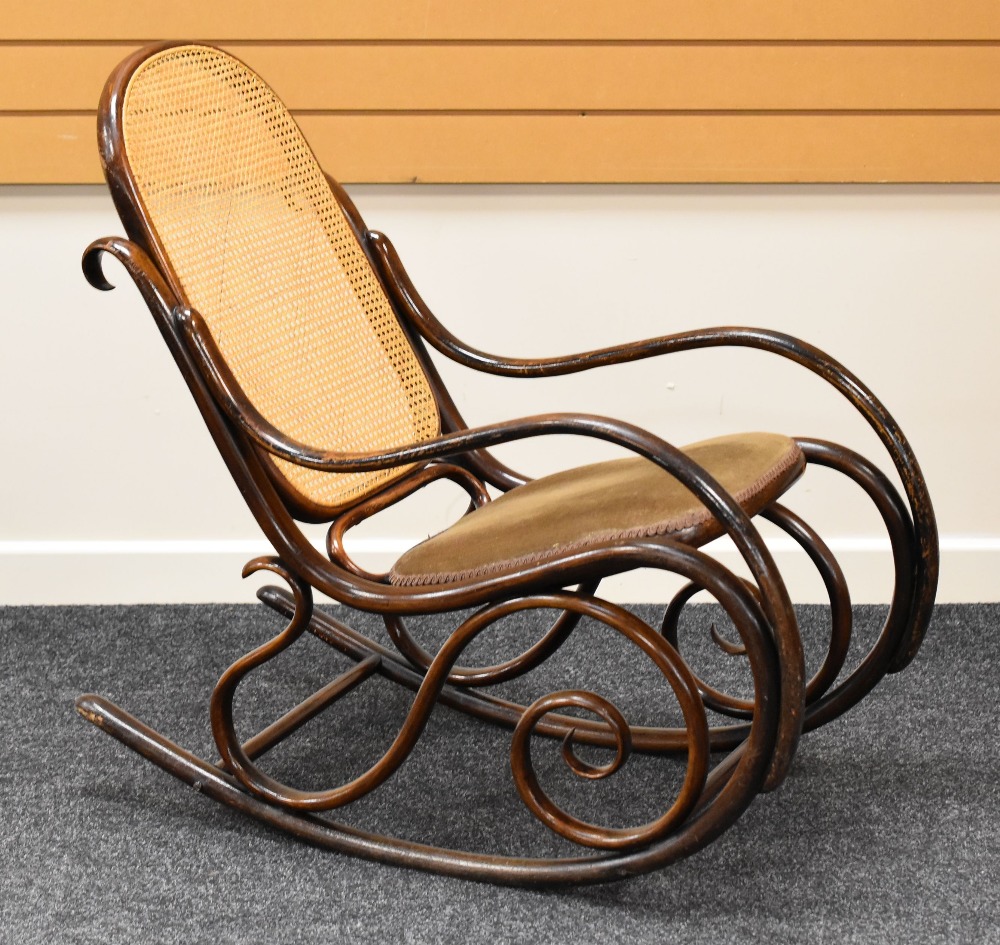 A DARK BENTWOOD ROCKING CHAIR with cushion seat and with a cane back support, 92 x 51 cms