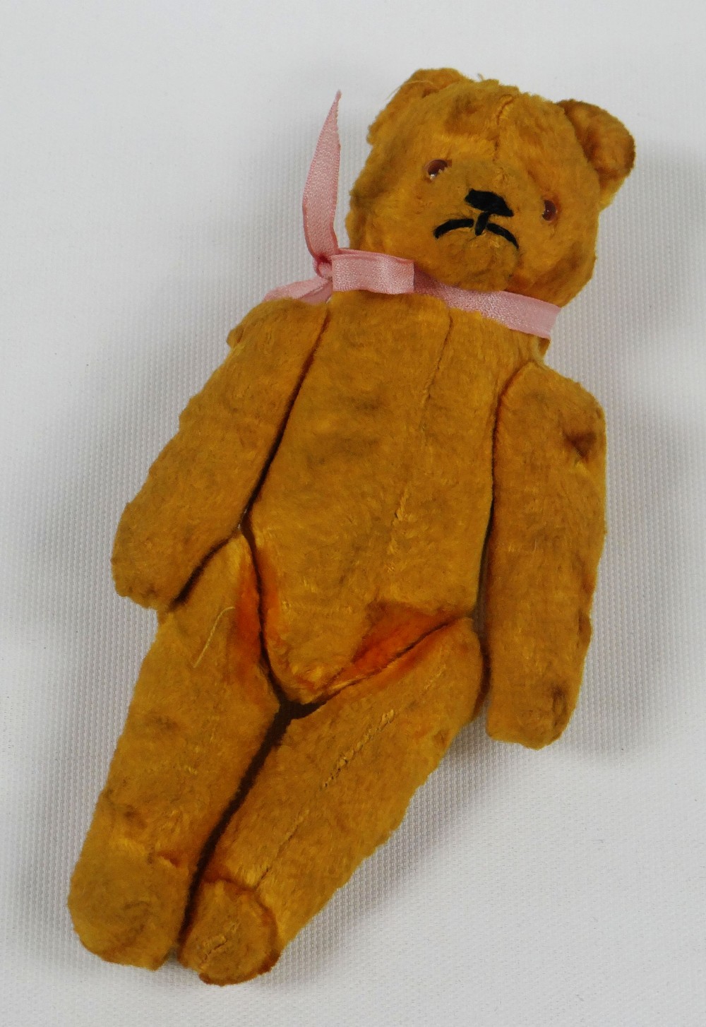 A SMALL EARLY TWENTIETH CENTURY GOLDEN PLUSH TEDDY BEAR with articulated limbs and glass eyes with