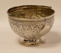A SILVER FOOTED BOWL WITH SWING-HANDLE profusely decorated in fine quality repousse work with a