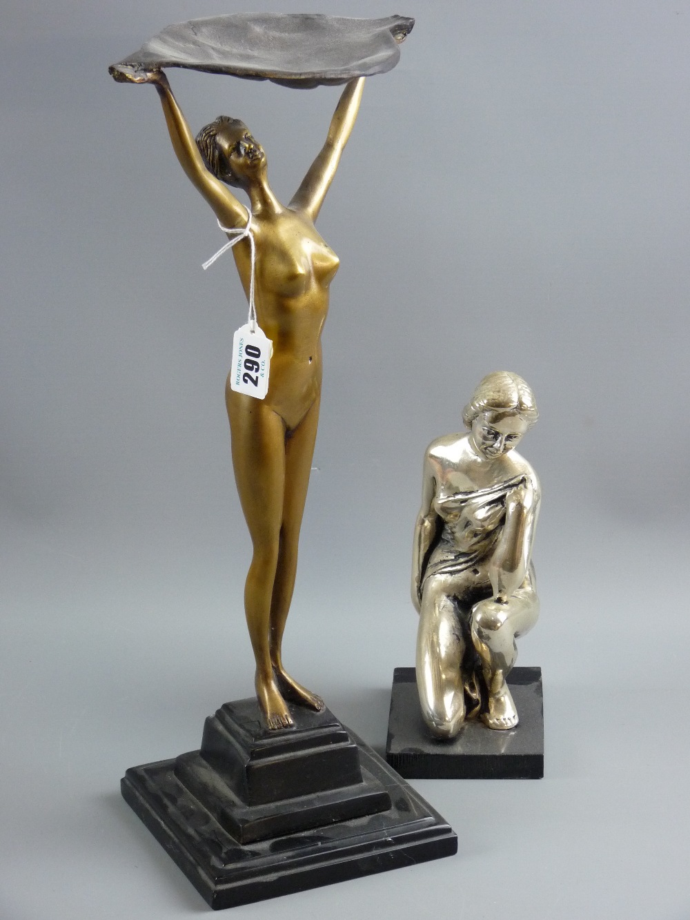 An Art Deco style gilt metal figure of a nude female holding a leaf shaped bowl aloft on a stepped