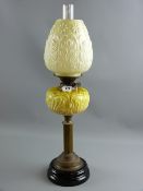 A Victorian oil lamp with relief moulded glass font on a brass column and black pottery base
