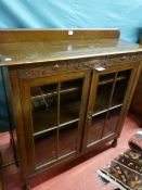 A circa 1930's oak bookcase, railback top over a carved frieze with twin glazed four panel doors and